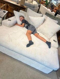 a young boy laying on top of a white bed in a room filled with furniture