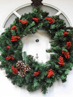 a wreath with red berries and pine cones hangs on the front door's wall