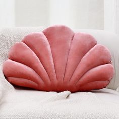 a pink scallop shaped pillow sitting on top of a white couch next to a window