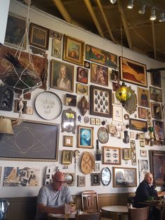 two men sitting at tables in front of a wall covered with pictures