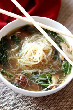 a white bowl filled with noodles and vegetables next to chopsticks on top of a table