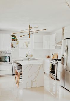 a white kitchen with marble counter tops and stainless steel appliances, along with an island in the middle