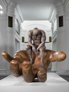 a man sitting on top of a wooden sculpture in a room with white walls and columns