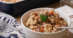 a white bowl filled with meat and vegetables on top of a wooden table next to a blue dish towel