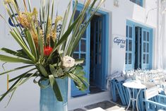 a blue vase filled with flowers sitting on top of a sidewalk next to tables and chairs