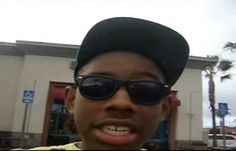 a young man wearing sunglasses and a hat in front of a building with palm trees