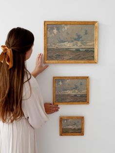 a woman is looking at some paintings on the wall and pointing to them with her hand