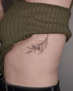 a woman's stomach with an olive branch tattoo on her lower back and side