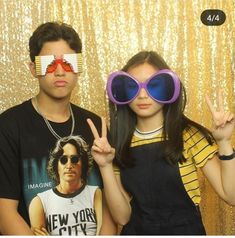 two people posing for a photo in front of a gold curtain with sunglasses on their faces