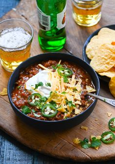 a bowl of chili with sour cream and tortilla chips on a wooden board