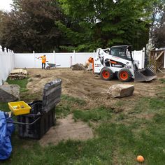 two men are working in the yard with construction equipment on the ground and behind them there is a large bulldozer