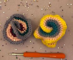 two crocheted objects are next to a knitting needle on a table with confetti sprinkles