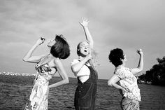 three women standing next to each other in front of the ocean with their arms up