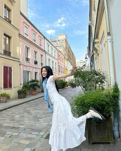 a woman in a white dress is leaning on a planter and posing for the camera