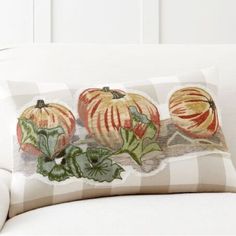 three pumpkins are on the back of a white couch with striped pillows and green leaves