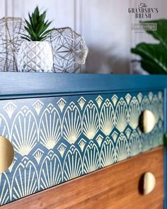 a blue dresser with gold knobs and an art deco design painted on it's drawers