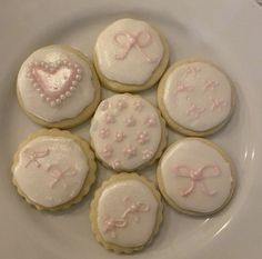 six decorated cookies on a white plate with pink bows and hearts in the shape of heart