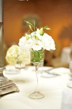 white flowers in a clear vase on a table with silverware and napkins around it