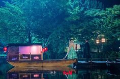 a man and woman are standing on the back of a boat in the water at night