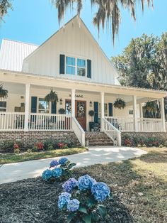 a white house with green shutters and blue flowers