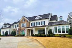 a large white house with lots of windows and bushes in the front yard on a cloudy day