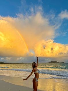 a woman standing on top of a sandy beach under a rainbow colored cloud filled sky