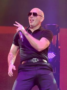 a bald man in black shirt and sunglasses on stage with his hand out to the side