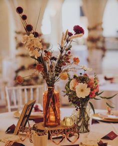 two vases filled with flowers sitting on top of a white tablecloth covered table