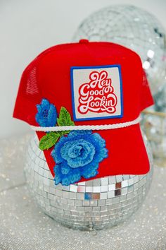 Maximize your style with this HEY GOOD LOOKIN FLORAL HAT. Embellished with a trendy hey good lookin patch and featuring blue floral accents and a custom red hat, this piece is sure to turn heads. Add a statement-making piece to your wardrobe. This hat is one-of-a-kind, created by our owner Stephanie. All orders are currently shipping within 14 business days. To receive item quicker, expedited shipping is available at checkout. Trendy Hats With Embroidered Patch, Trendy Red Trucker Hat With Short Brim, Red Snapback Baseball Cap For Spring, Trendy Red Trucker Hat With Flat Brim, Trendy Red Trucker Hat, Trendy Trucker Hats, Hat Bar, Custom Trucker Hats, Glitter Spray