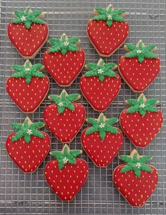 twelve decorated cookies arranged in the shape of strawberries on a cooling rack with green bows