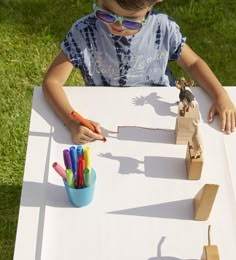 a little boy sitting at a table with paper and scissors