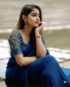 a woman in a blue sari sitting on the ground with her hand under her chin