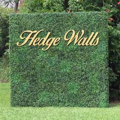 the hedge walls sign is in front of some trees and bushes with gold lettering on it