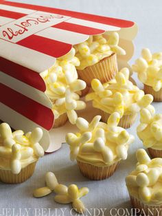 cupcakes with white frosting and candy in the shape of popcorn boxes on a table