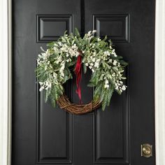 a wreath with white flowers and greenery hangs on the front door to welcome guests