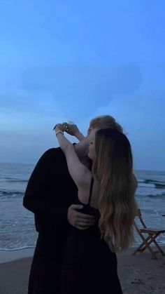 two people are kissing on the beach at dusk