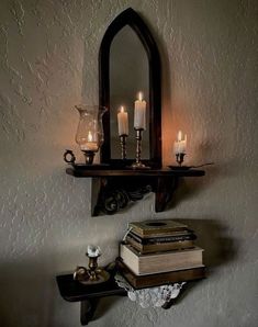 some books and candles are sitting on a shelf in front of a mirror that is hanging from the wall