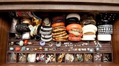 a drawer filled with lots of jewelry on top of a wooden table next to a wall