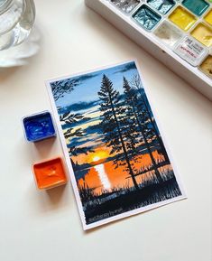 a table with paint, watercolors and an image of the sun setting in the sky