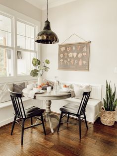 a table with two chairs and a bench in front of a window next to a potted plant