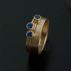 This unique design features three 3mm blue Montana sapphires bezel set on 1mm bands with a 3mm band. All in 14k yellow gold.The blue Montana sapphires look striking in yellow gold.The sculptural aspect of this design makes it even more unique as you can arrange the bands in different combinations.Please allow 2 weeks for creation. Gold Sapphire Stackable Rings With Bezel Setting, Yellow Gold Sapphire Stackable Rings With Bezel Setting, Gold Stackable Rings With Sapphire Bezel Setting, Yellow Gold Stackable Sapphire Ring, Gold Sapphire Three Stone Jewelry, Gold Sapphire Jewelry With Three Stones, Gold Sapphire Stackable Rings In Fine Jewelry Style, Yellow Gold Sapphire Ring With Tension Setting, Stackable Gold Sapphire Ring In 14k Gold