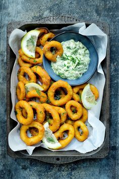 some onion rings are on a tray with dip and lemon wedges