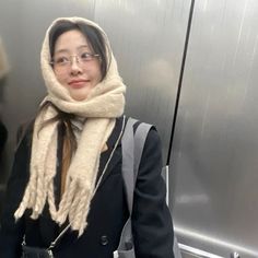 a woman wearing glasses and a scarf on an escalator with her hand in her pocket