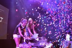 two girls are djing on stage with confetti falling from the ceiling behind them