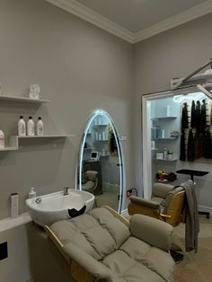 a hair salon with an oval mirror and white sink in the center, along with two tan leather recliners