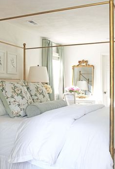 a bed with white linens and pillows in a bedroom next to a mirror on the wall