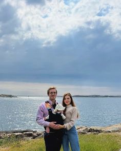 a man and woman standing next to each other in front of a body of water