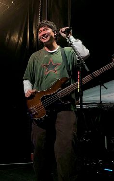 a man holding a guitar and singing into a microphone while standing in front of a stage