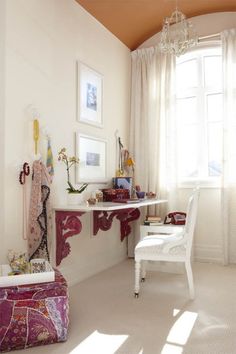 a white chair sitting in front of a desk next to a window with lots of pictures on it