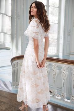 a woman in a white dress standing on a wooden floor next to a railing and window